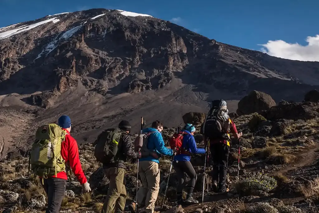 Climbers hiking over rocky ground toward Kilimanjaro