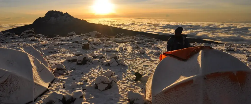 A climber watching the sunrise from a tent above the clouds