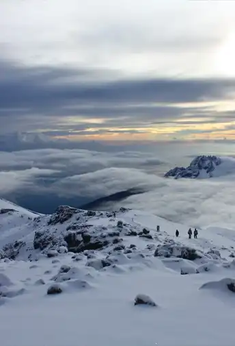 Climbers crossing a snowfield above the clouds
